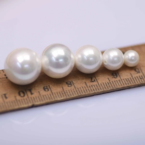 Close-up of white glass pearls in various sizes on a wooden ruler for measurement