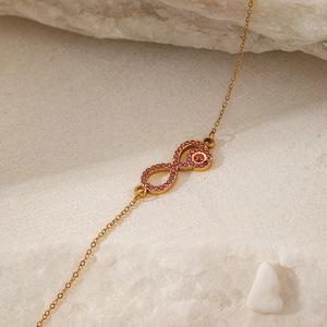 Golden infinity necklace with sparkling pink zircons shown on a natural stone background