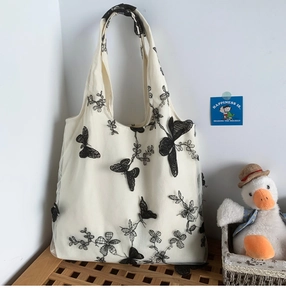 Close-up of white canvas tote featuring intricate black lace butterfly and floral embroidery