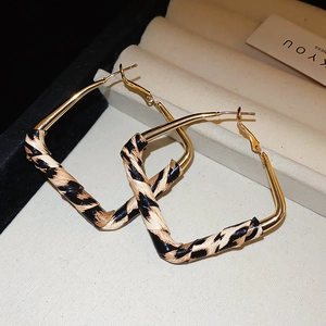 Detailed view of large gold square earrings with leopard print leather wrap on jewelry tray