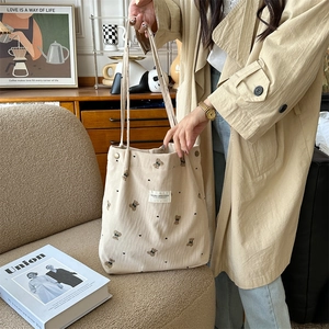 Detail of cream corduroy tote bag with bear embroidery held by model in soft light