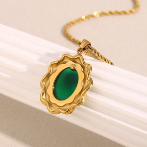 Détail d'un pendentif ovale avec pierre verte, cadre doré ondulé et chaîne torsadée