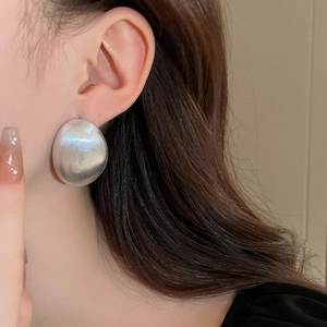 Primo piano dettagliato di un orecchino ovale minimalista in metallo spazzolato argento.