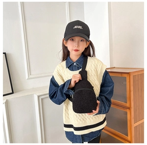 Close-up of a child wearing the plush black crossbody bag in a cozy indoor setting
