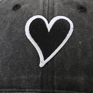 Detail of black heart embroidery with white borders on washed cotton baseball cap