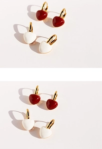 Detailed view of red and white enamel heart earrings with golden metal hoop closures
