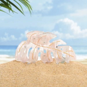 Detail of pink leaf hair claw with gold veins and rhinestones on a sunny beach