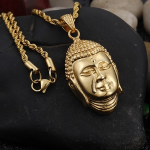 Macro shot of gold Buddha head pendant with rope chain on a dark stone background