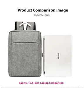 Grey business laptop backpack with USB port shown next to a 15.6 inch computer for scale