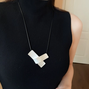 Close-up of irregular white geometric pendant with black leather cord on model