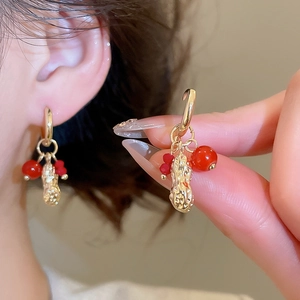 Close-up of gold peanut charm earrings with red beads and luxury metal texture details