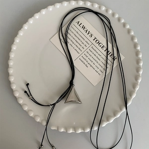 Detailed view of silver triangular cone pendant on black cord over white ceramic plate