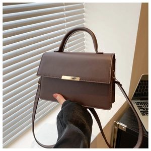 Close-up of a vintage brown leather crossbody square bag with a sleek metal bar lock closure