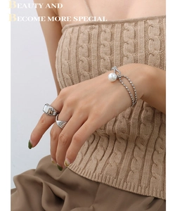 Close-up of minimalist pearl pendant bracelet and silver rings on model wearing a sweater