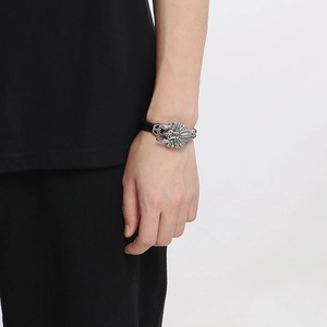 Detail of woven black leather bracelet featuring a silver Indian skull and feather charm
