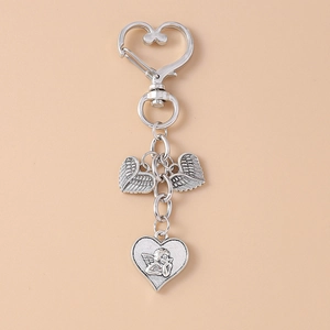 Detail of silver angel wing keychain with rhinestone heart pendants on beige background
