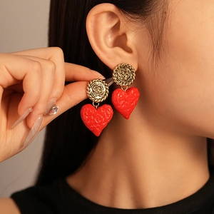 Close-up of vintage deep red heart earrings with golden flower studs worn by a model