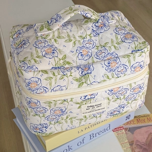 Floral quilted toiletry bag with blue flower pattern and top handle on books