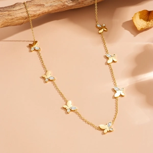 Collana a farfalla dorata con zirconi bianchi su espositore in legno naturale
