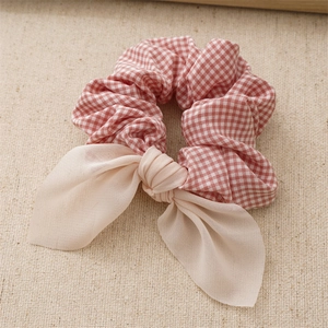 Close-up of a red and white plaid scrunchie with a beige fabric bow accessory