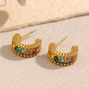 Close-up of gold C-shaped hoop earrings with colorful inlaid zircons on beige background