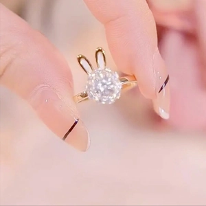 Golden rabbit head ring with clear gemstone and white enamel detailing held by hand