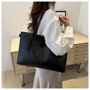 Detailed shoulder view of a black soft leather tote bag with slim straps in a home setting