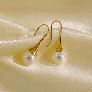 Detail view of pearl earrings with gold hooks resting on luxury champagne silk fabric