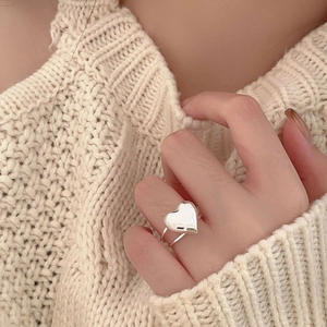 Close-up of 925 sterling silver heart ring on finger against beige knit sweater