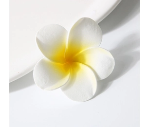 Detail of realistic white and yellow plumeria flower clip on a white ceramic plate
