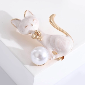 Detailed view of white enamel cat brooch with gold accents and large pearl on a display stand