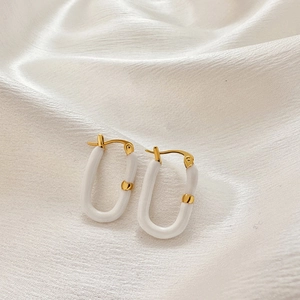 Detailed shot of U-shaped gold earrings with white enamel on luxury silk background