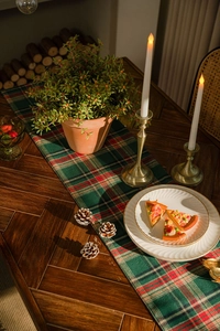 Close-up of a festive red and green plaid table runner with pine cones and candles decor