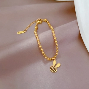 Dettaglio del bracciale dorato a sfere con ciondolo a coniglio su seta viola chiaro