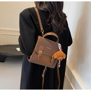 Back view of a retro brown leather backpack with a plush puppy charm on a model