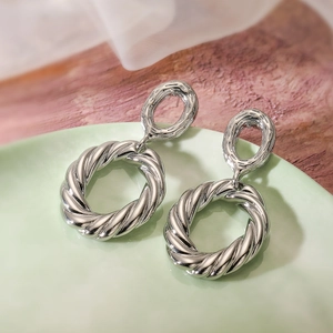 Minimalist silver geometric twist drop earrings shown on a decorative pale green tray