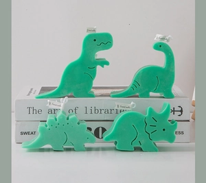 Detailed close-up of green dinosaur-shaped scented candles on minimalist book props