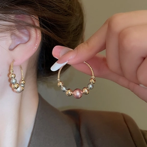 Detailed shot of twisted metal hoop earrings with colorful pearl beads on fingers