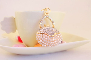 Macro detail of golden handbag keychain with pearls and rhinestones on white backdrop