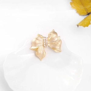 Detailed view of golden ribbon brooch with brushed texture and elegant pearls in a dish