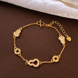 Détail d'un bracelet doré orné de breloques gourde et pièces serties de zircons