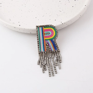 Close-up of R-shaped brooch with rainbow embroidery, rhinestones and tassel detail