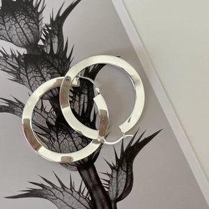 Macro shot of large polished S925 sterling silver hoop earrings on artistic floral card