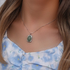 Close-up of a silver necklace featuring an oval green gemstone pendant on the model