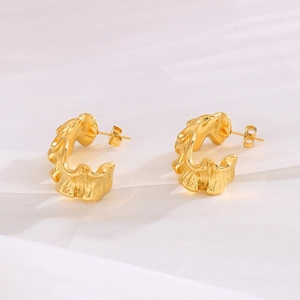 Macro detail of gold-plated C-shaped earrings with irregular wavy texture on fabric