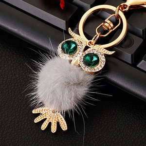 Close-up of owl keychain with sparkling green gemstone eyes and soft grey fur ball detail
