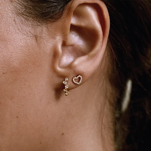 Close-up of golden heart stud and curved zirconia earring set worn on ear