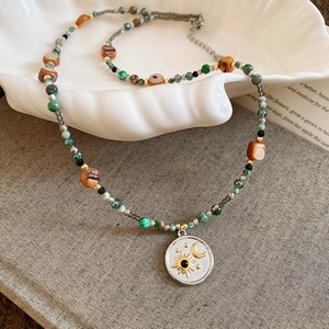 Détail d'un collier de perles avec pendentif lune et étoile sur un plateau coquillage