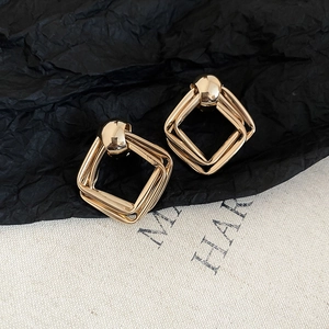 Macro shot of geometric gold metal square earrings with glossy layered finish and stud top
