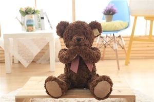 Detail of dark brown curly plush teddy bear with a red checkered bow on wood tray